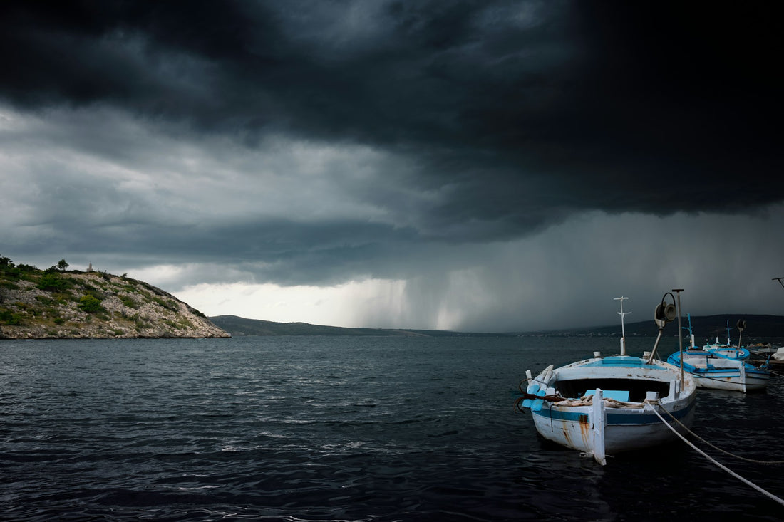 Dunkle Sturmwolken über dem Meer, vorne ein kleines Boot am Ufer