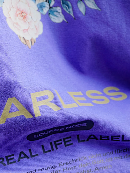 Detailaufnahme des violetten Source Mode Fearless T-Shirts mit goldenem FEARLESS Print, Source Mode und Real Life Label Schriftzug sowie floralen Elementen. Christliche Streetwear als Symbol für Mut, Stärke und Gottes Führung.