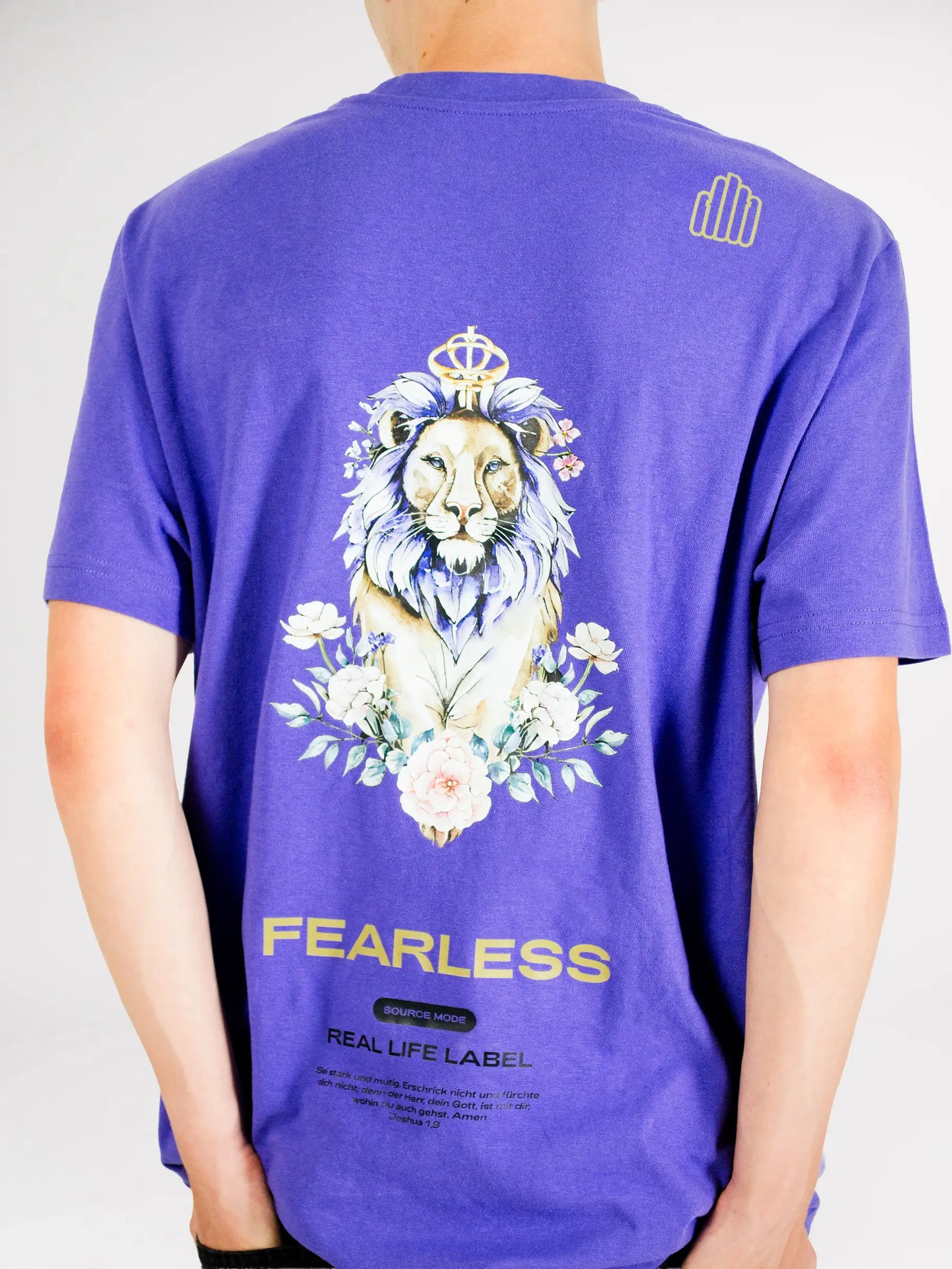Rückenansicht eines Models im violetten Source Mode Fearless T-Shirt mit großem gekrönten Löwen-Backprint, floralen Elementen, goldenem FEARLESS und Real Life Label Schriftzug. Christliche Streetwear als Symbol für Mut, Stärke und Gottes Führung.