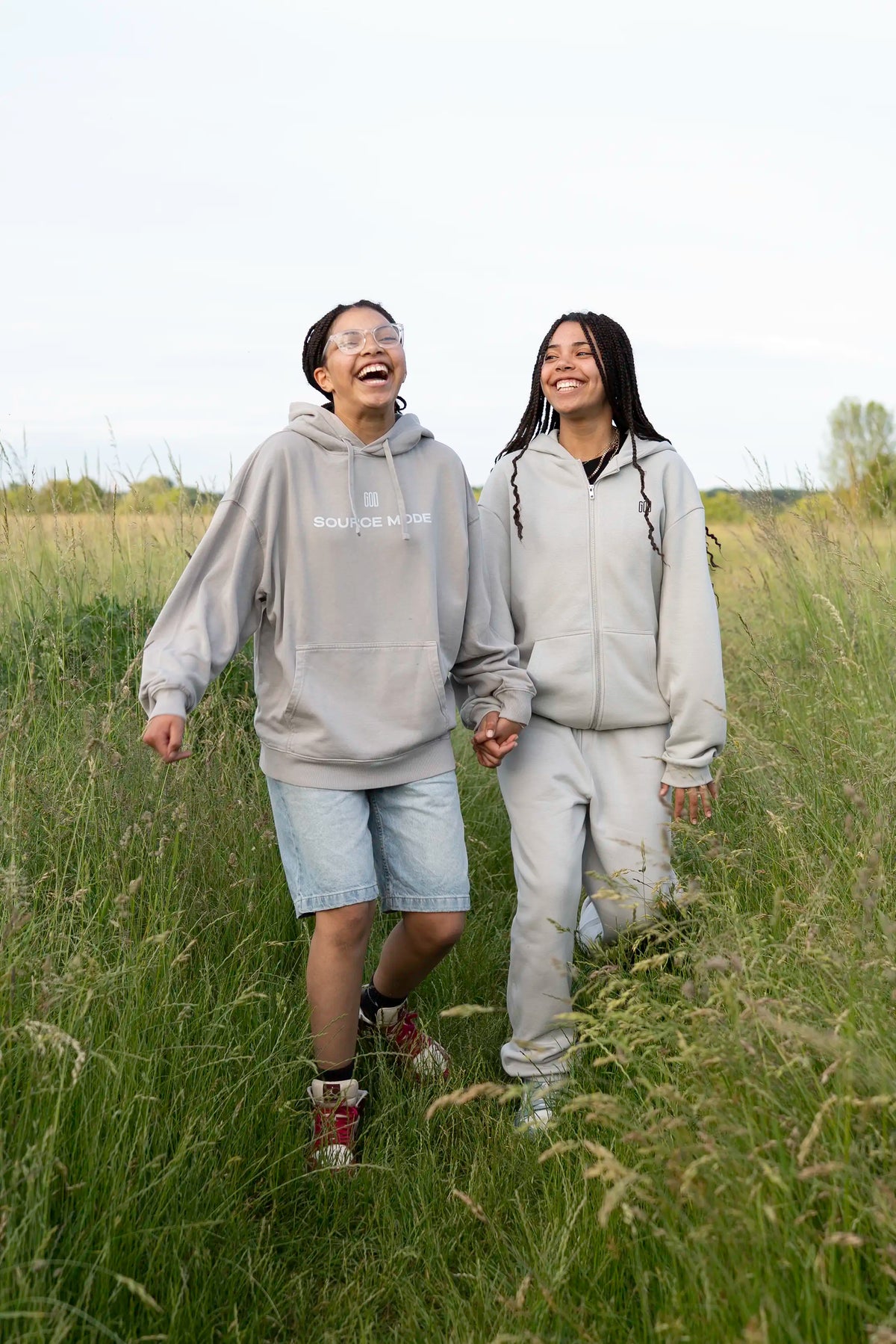 Lifestyle: zwei Models im Open Source Ticket Hoodie in Misty Gray auf einer Sommerwiese